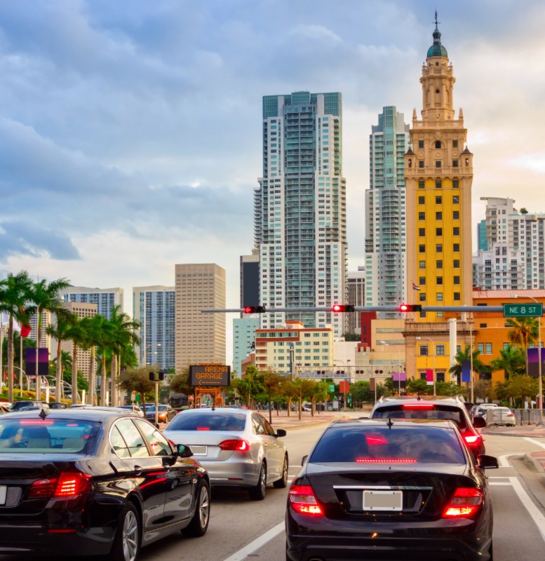 Multiple cars at a stop light in downtown Miami where people are wondering why auto insurance rates are going up.