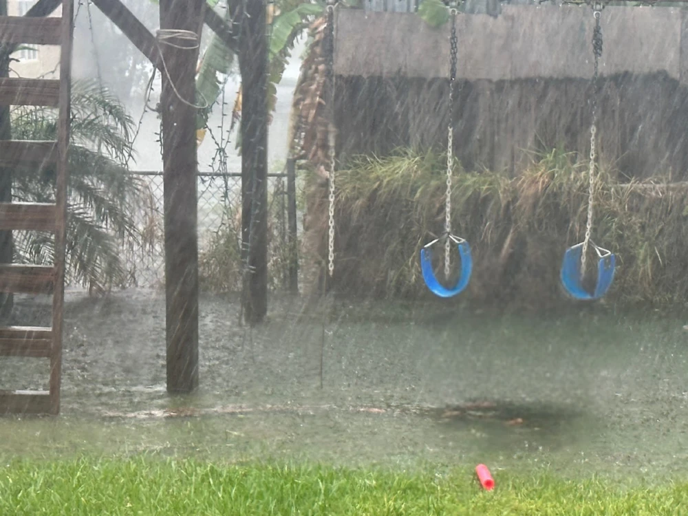 Rain is pouring down on an empty park with swings.