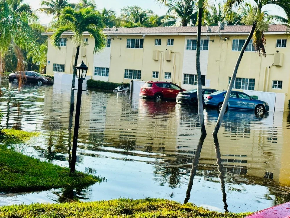 Image of two story building with a flooded parking lot. several cars are partially submerged.